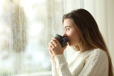woman drinking from mug looking out rainy window